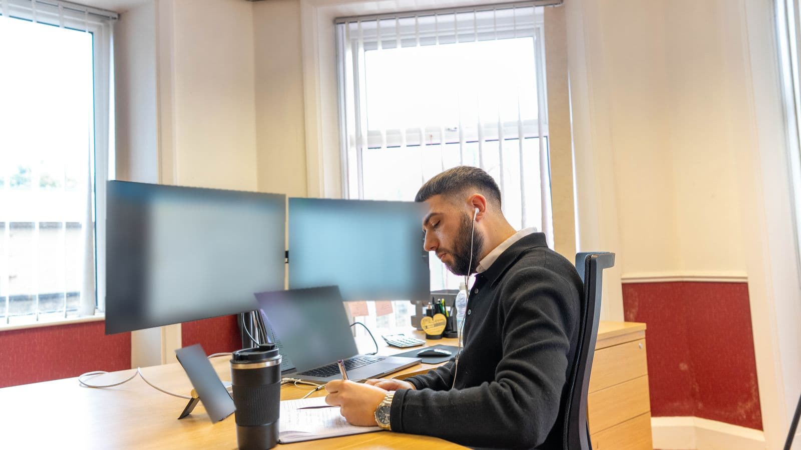 A Motorhome Pig team member writing notes in a notebook at a desk with two monitors and a laptop, in the company's Halifax office