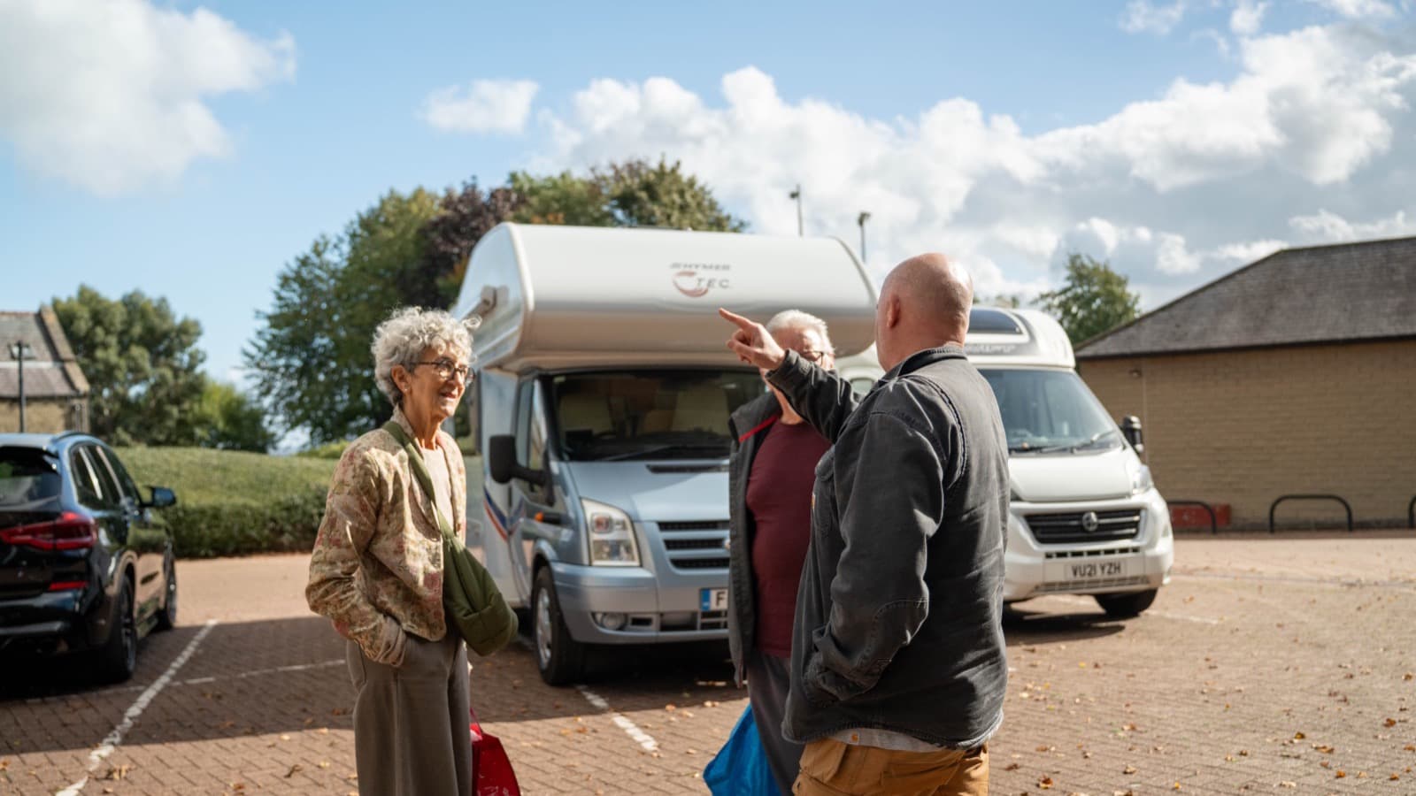 Two customers talking with a member of the Motorhome Pig team beside a Ford-based Hymer motorhome in the car park at the Halifax office