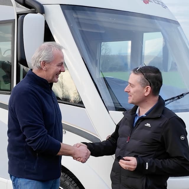 Seller and buyer shaking hands in front of a sold motorhome