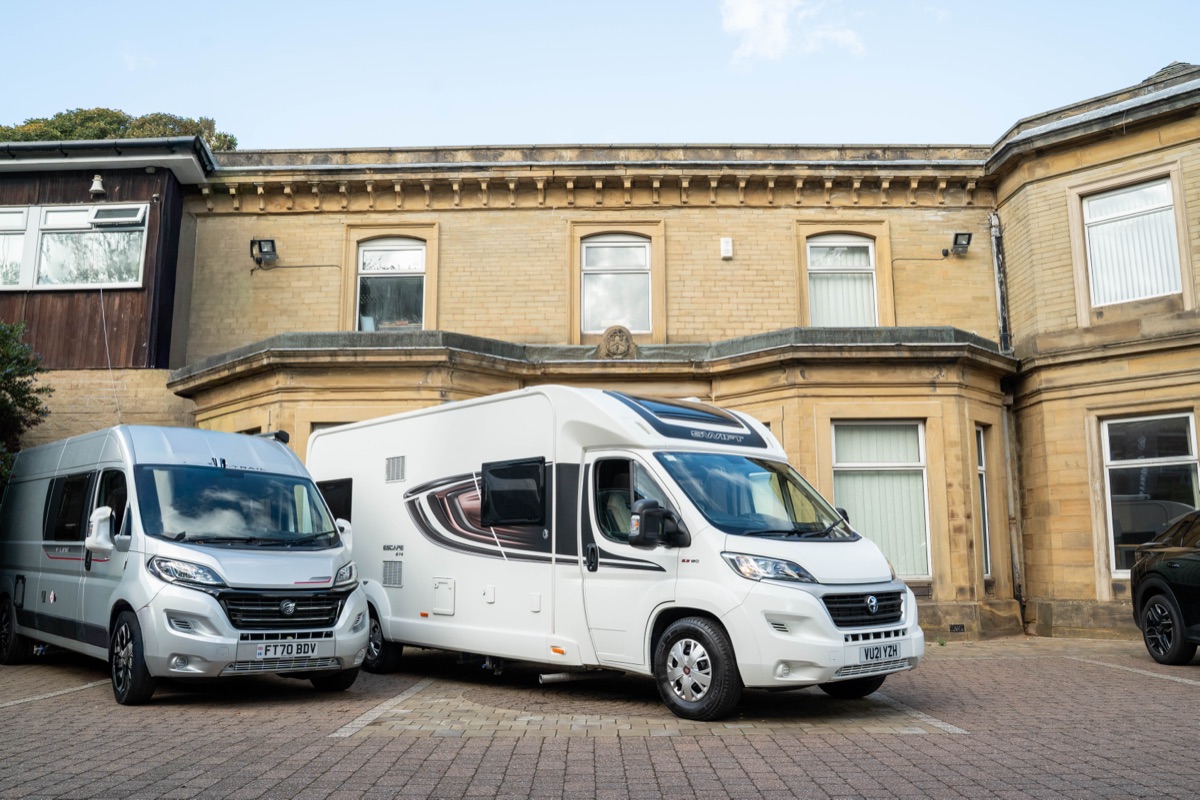 A silver panel-van campervan parked beside a larger white coachbuilt motorhome outside Motorhome Pig's office