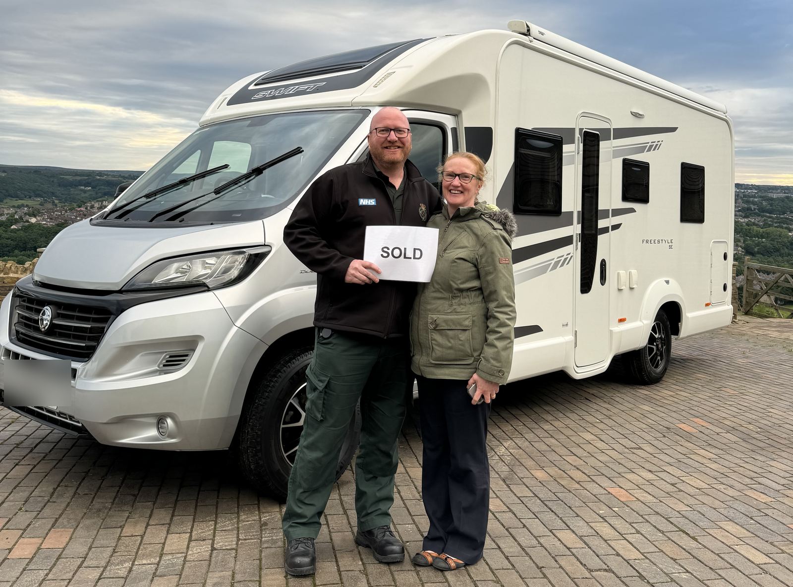 A couple standing beside their Swift Freestyle motorhome holding a SOLD sign after selling through Motorhome Pig