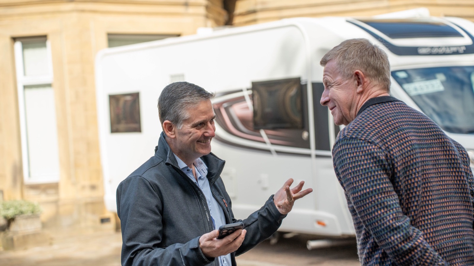 Two men talking beside the side of a white coachbuilt motorhome outside Motorhome Pig’s stone office building in Halifax