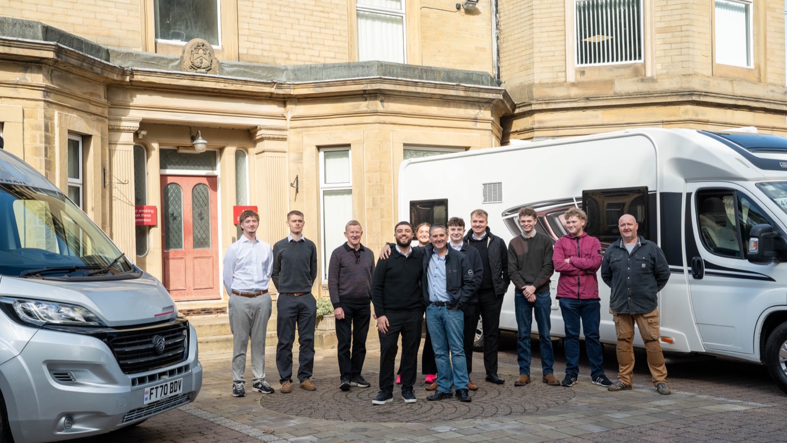 The Motorhome Pig team standing together outside the company's stone office building in Halifax, between a silver panel van and a white motorhome