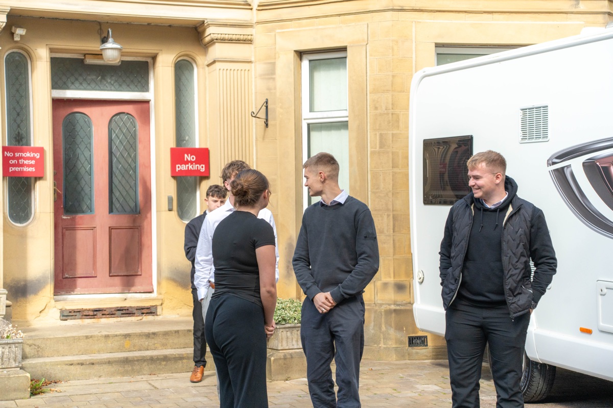 Members of the Motorhome Pig team chatting in a small group outside the office front door, beside a white motorhome