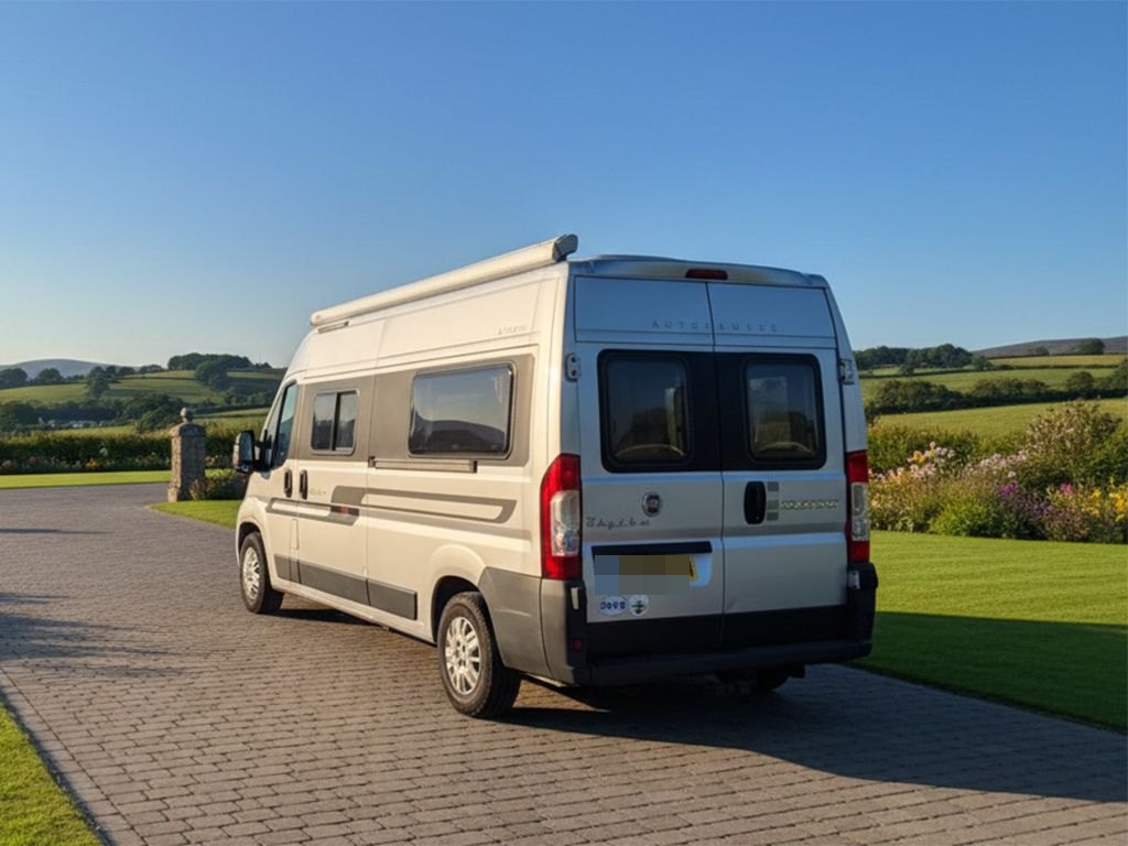 Rear three-quarter view of the Autocruise Rhythm parked on a block-paved driveway with green countryside behind (number plate digitally obscured)