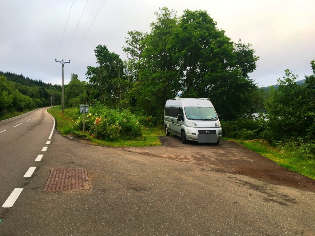 The Autocruise Rhythm parked in a layby beside a wooded Highland road and loch, on an overcast day