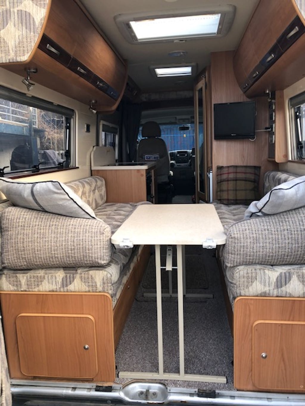 The bright interior of the Autocruise Rhythm with the rear lounge set up around a table, looking forward toward the cab