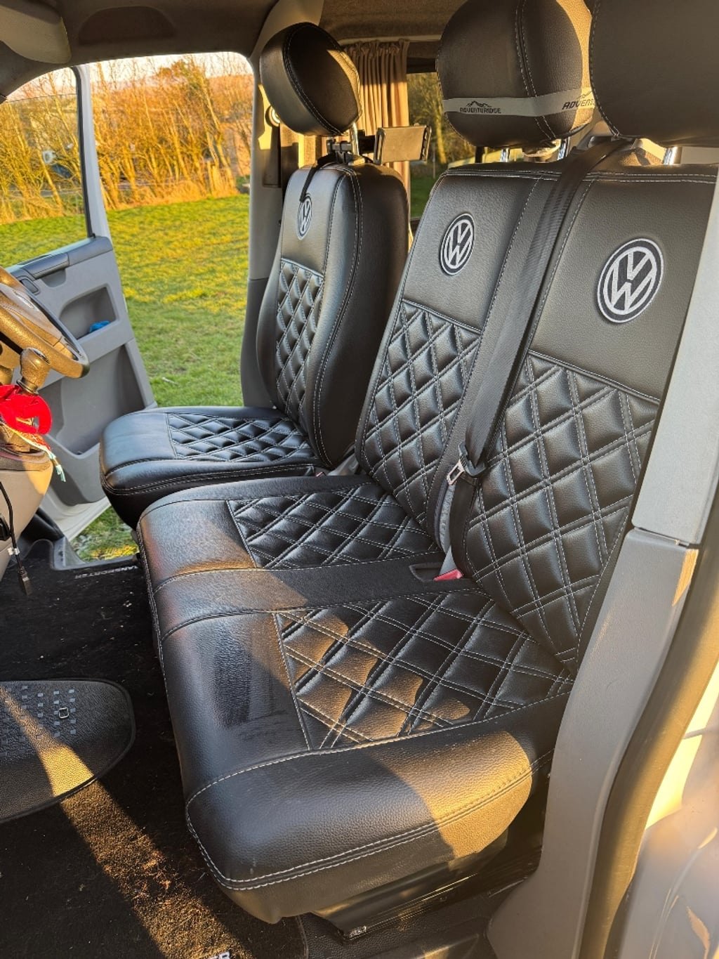 The cab of the VW Transporter campervan with black quilted diamond-stitch seat covers carrying embroidered VW roundels on the headrests and seat backs