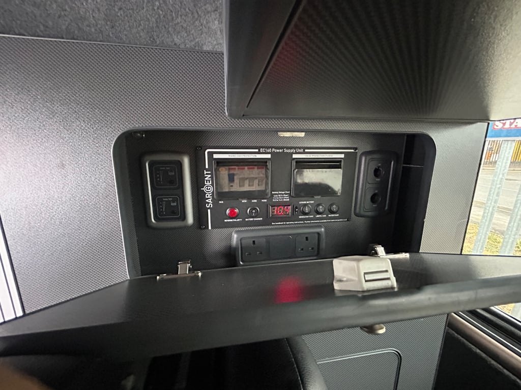 A Sargent power supply unit control panel with a pair of 230V sockets, mounted inside a grey cabinet in the campervan