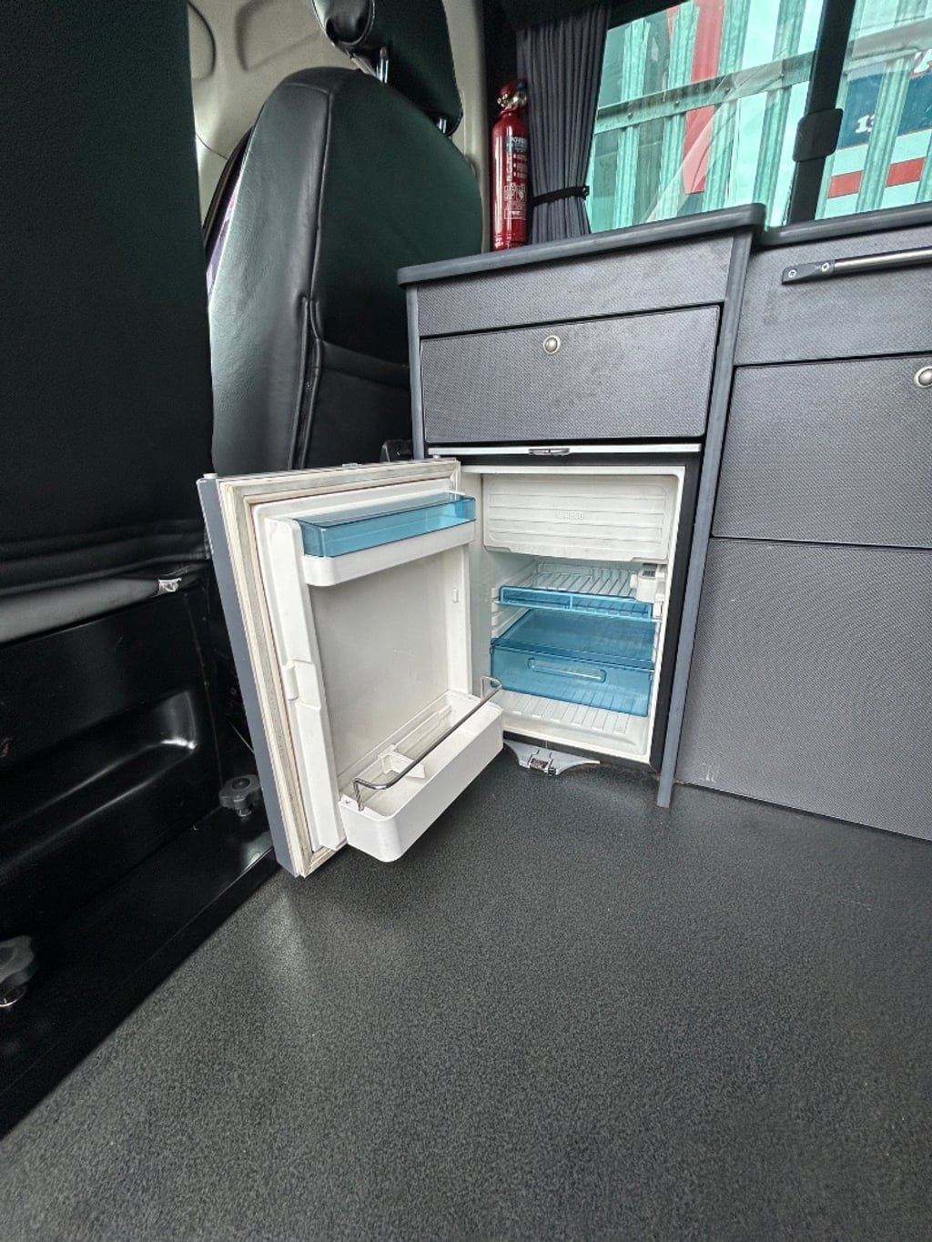 An open white fridge built into the campervan's kitchen unit next to the worktop