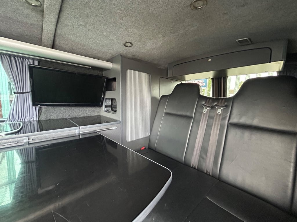 The rear living area of the campervan looking forward past the kitchen unit toward the cab, with striped curtains drawn