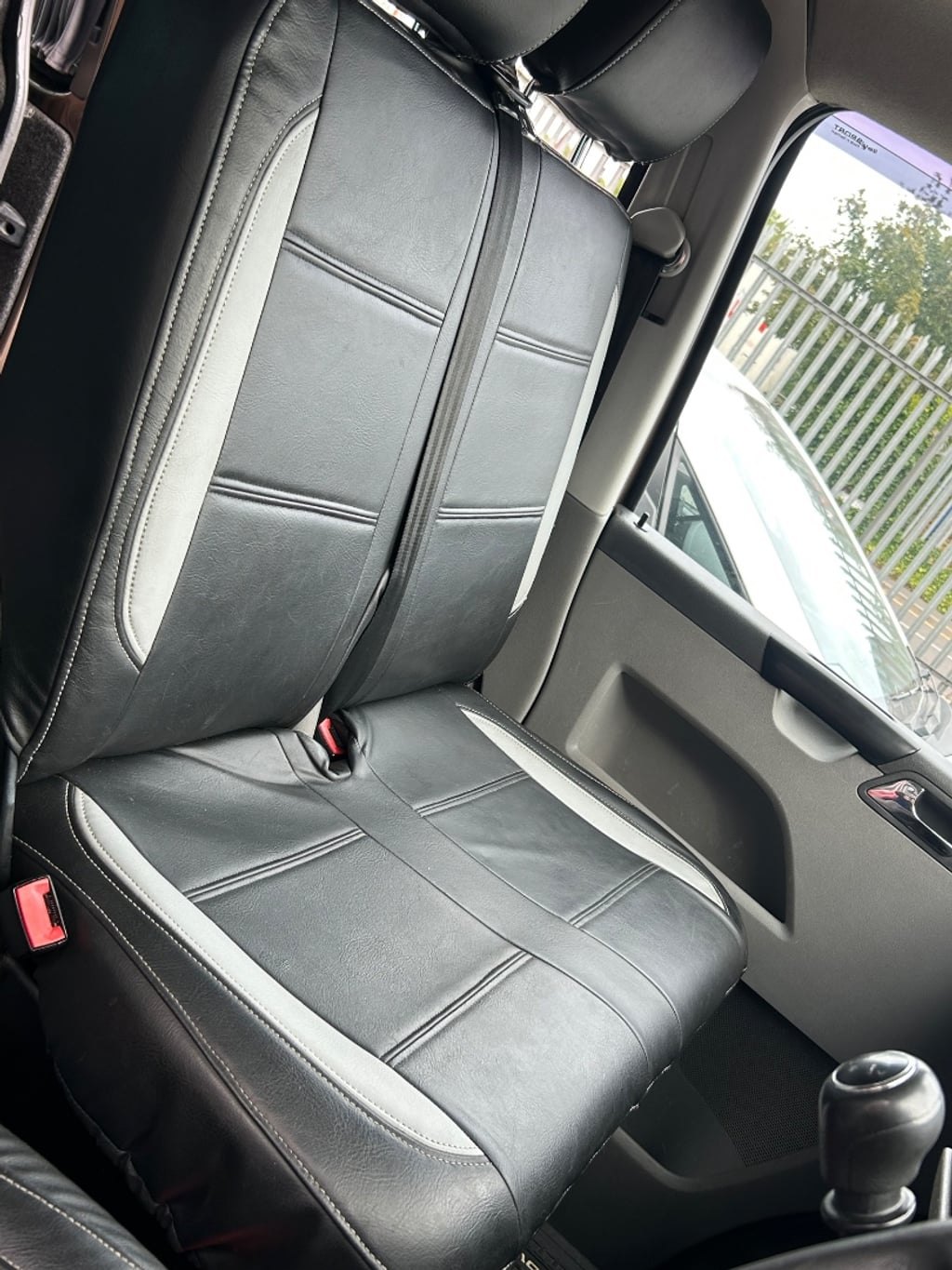 The rear bench seat of the campervan in dark leather with white piping, folded upright in its seating position