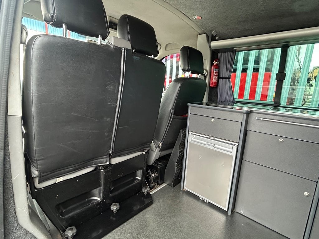 Storage lockers and a grey cupboard unit inside the campervan, with the side windows and blinds visible