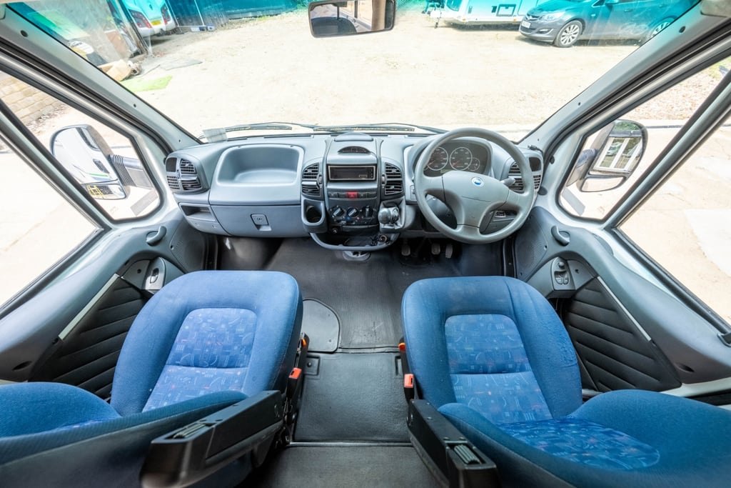 The cab of the Chausson Welcome 85 with blue swivel captain's seats, steering wheel and dashboard