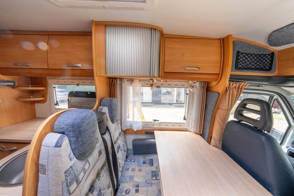 The dinette of the Chausson Welcome 85 with a table extended, blue upholstered seating and a window