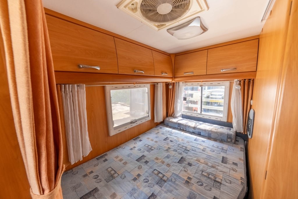 The fixed rear double bed of the Chausson Welcome 85, with overhead lockers, curtains and a ceiling fan