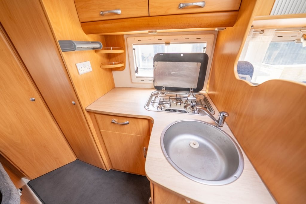 The kitchen area of the Chausson Welcome 85 with a stainless steel sink, gas hob under a glass lid and light wood cabinetry