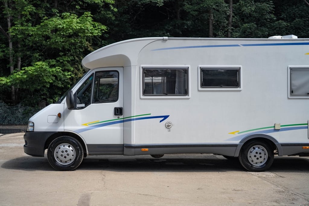 Side profile of the white Chausson Welcome 85 motorhome showing its full length, blue and green graphics and habitation door