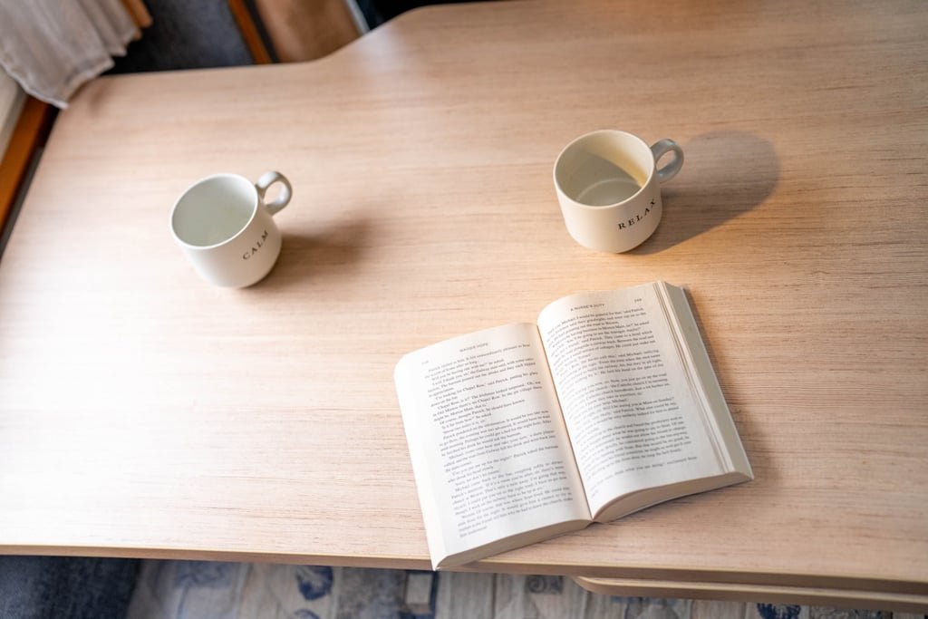 Two mugs and an open book on the wooden table inside the Chausson Welcome 85