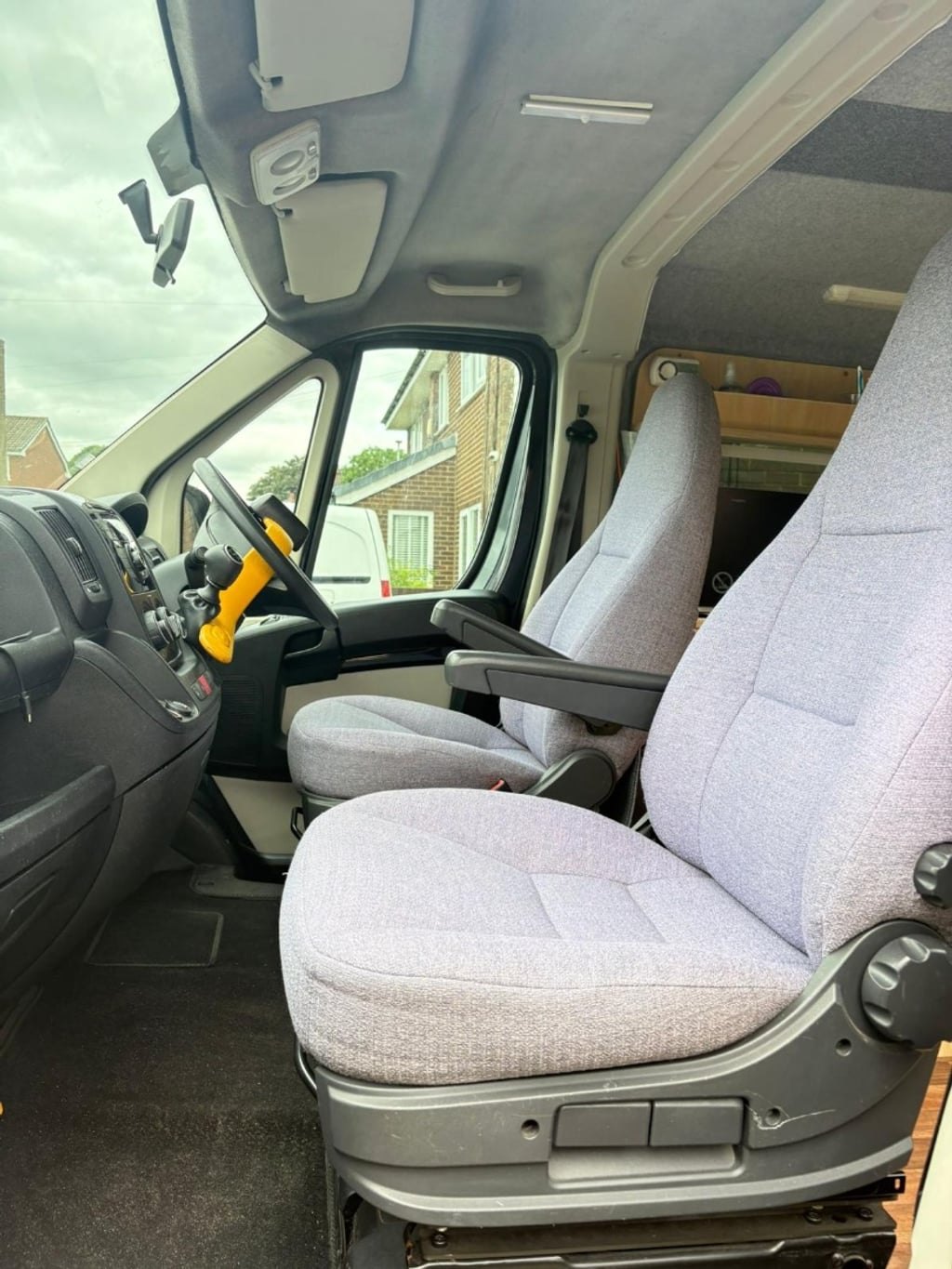 The cab of the Peugeot Boxer showing the steering wheel with a yellow security lock and the grey swivel passenger seat