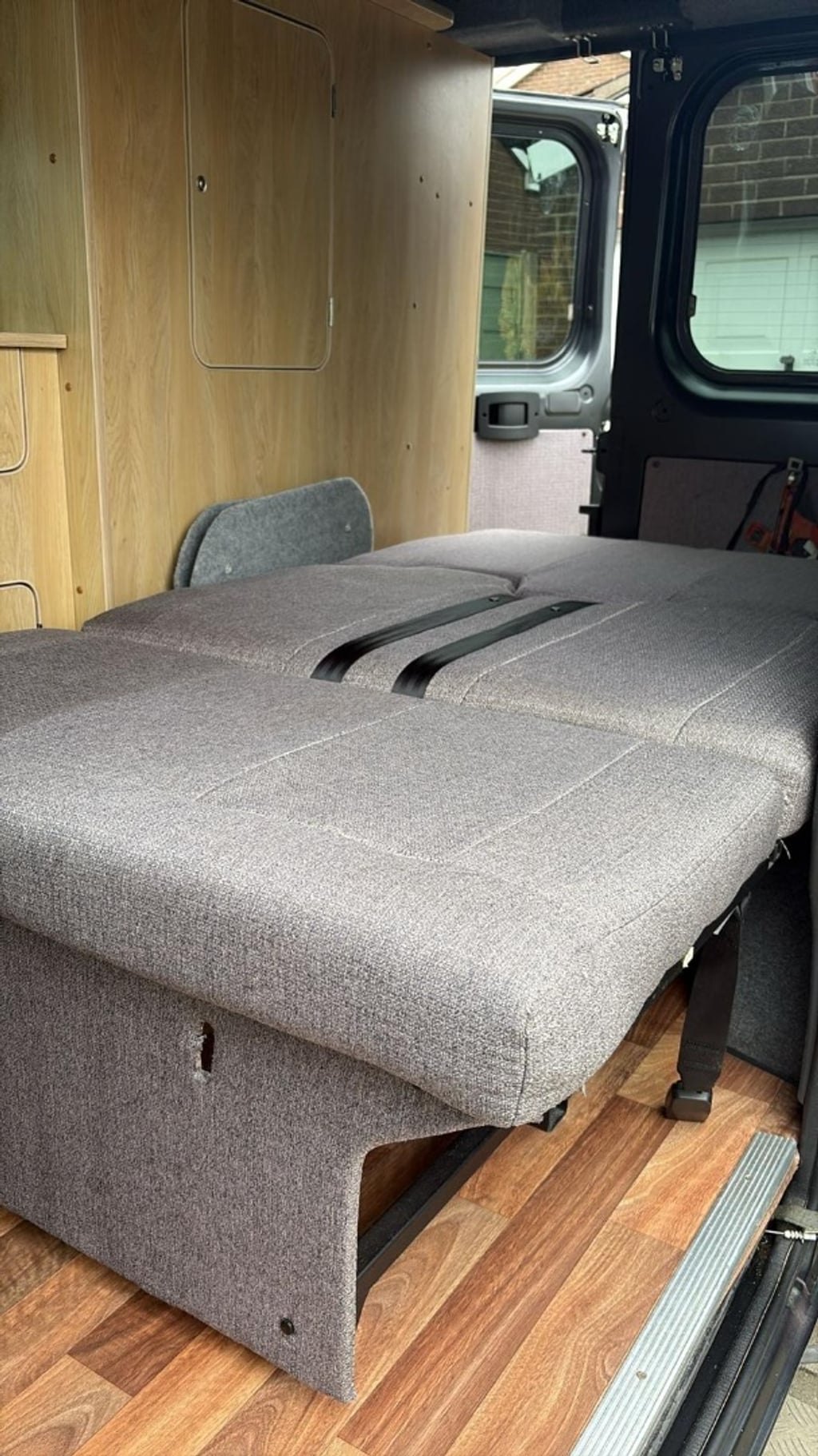 The rock and roll bed folded flat into a double bed with a grey mattress, on a wooden floor beside the rear doors