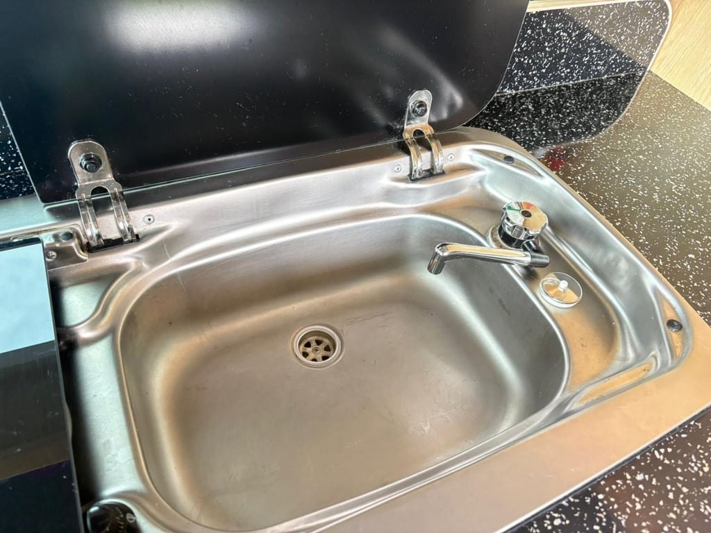 A stainless steel sink with a folding tap set into a black speckled worktop