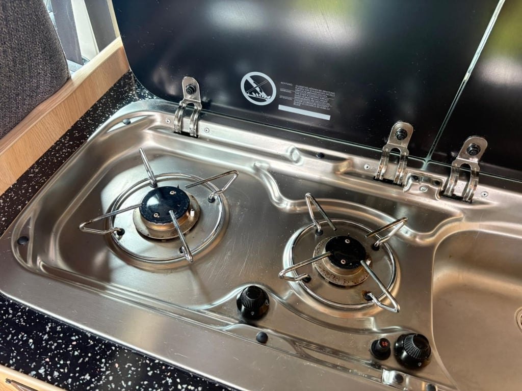 A stainless steel twin gas hob set into a black speckled worktop with the glass lid raised