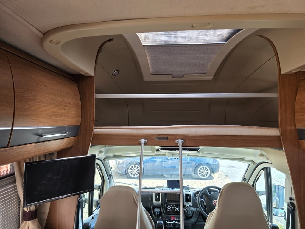 Interior of the Auto-Trail Cherokee looking towards the cab, with a large rooflight above the overcab bed, a swing-out TV on the left and the Fiat Ducato dashboard visible through the gap