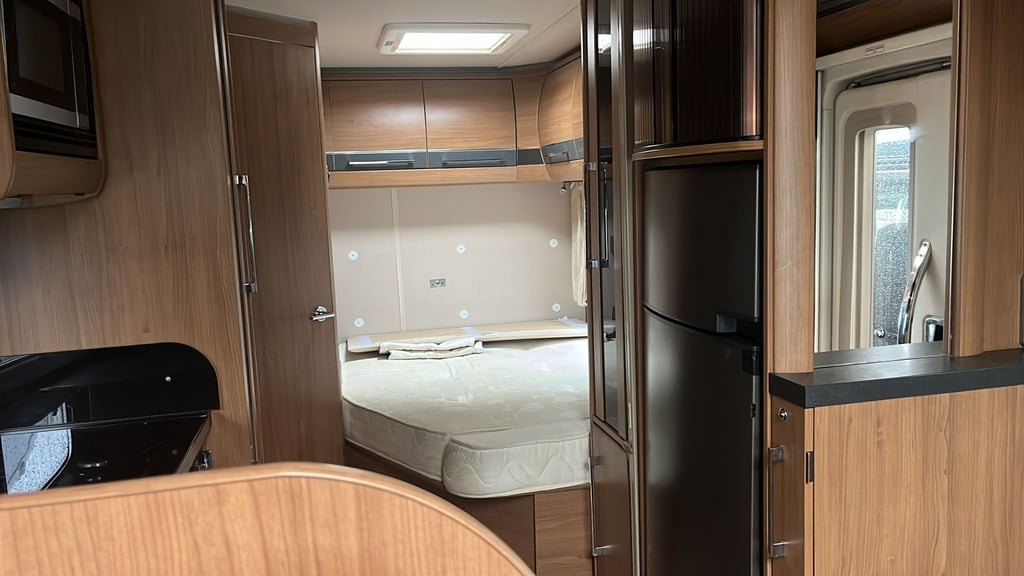 The fixed French bed at the rear of the Auto-Trail Cherokee seen from the lounge, with a tall wardrobe, overhead lockers and the tall fridge beside the doorway