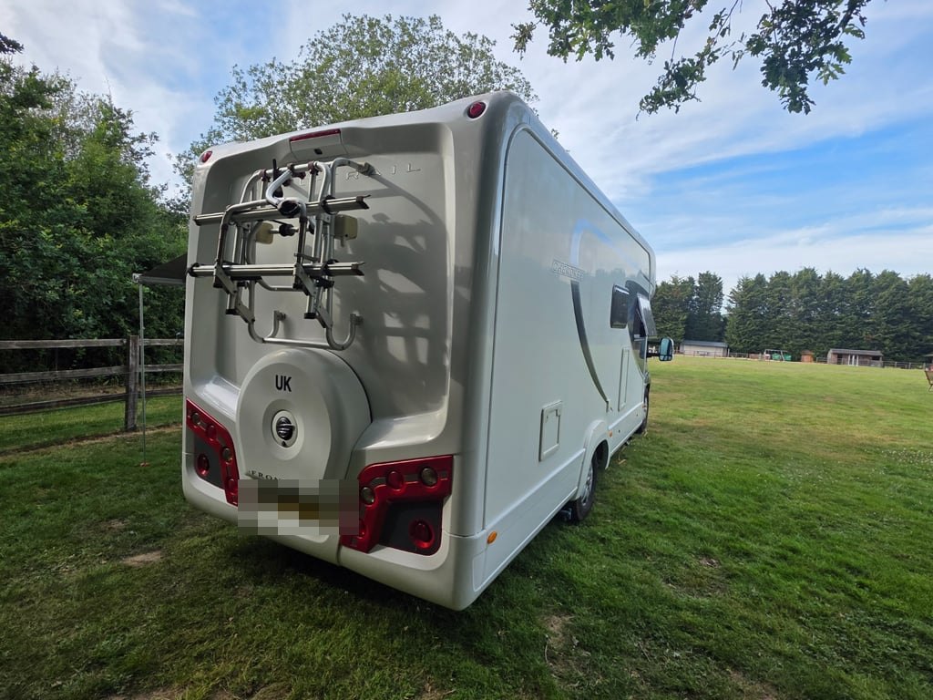 Rear view of the Auto-Trail Cherokee on a grass pitch showing the bike rack, the spare wheel cover, a UK sticker and the rear light clusters (number plate digitally obscured)