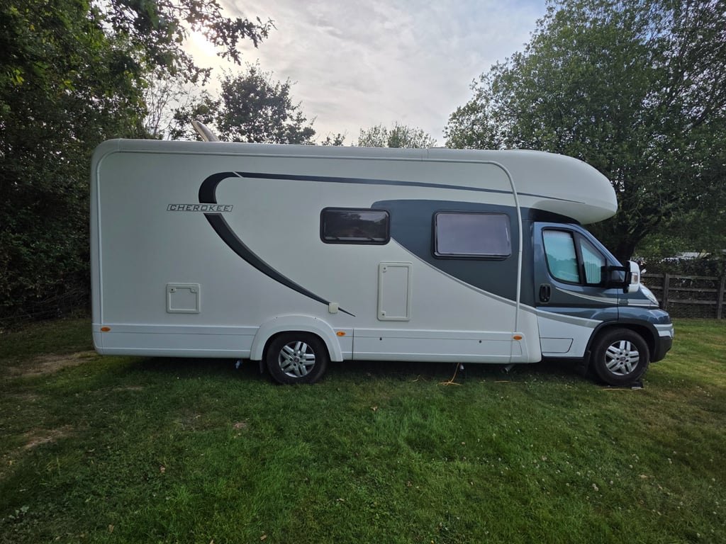 Side profile of the Auto-Trail Cherokee on grass, showing the full length of the white coachbuilt body with the Cherokee decal and grey swoosh graphic