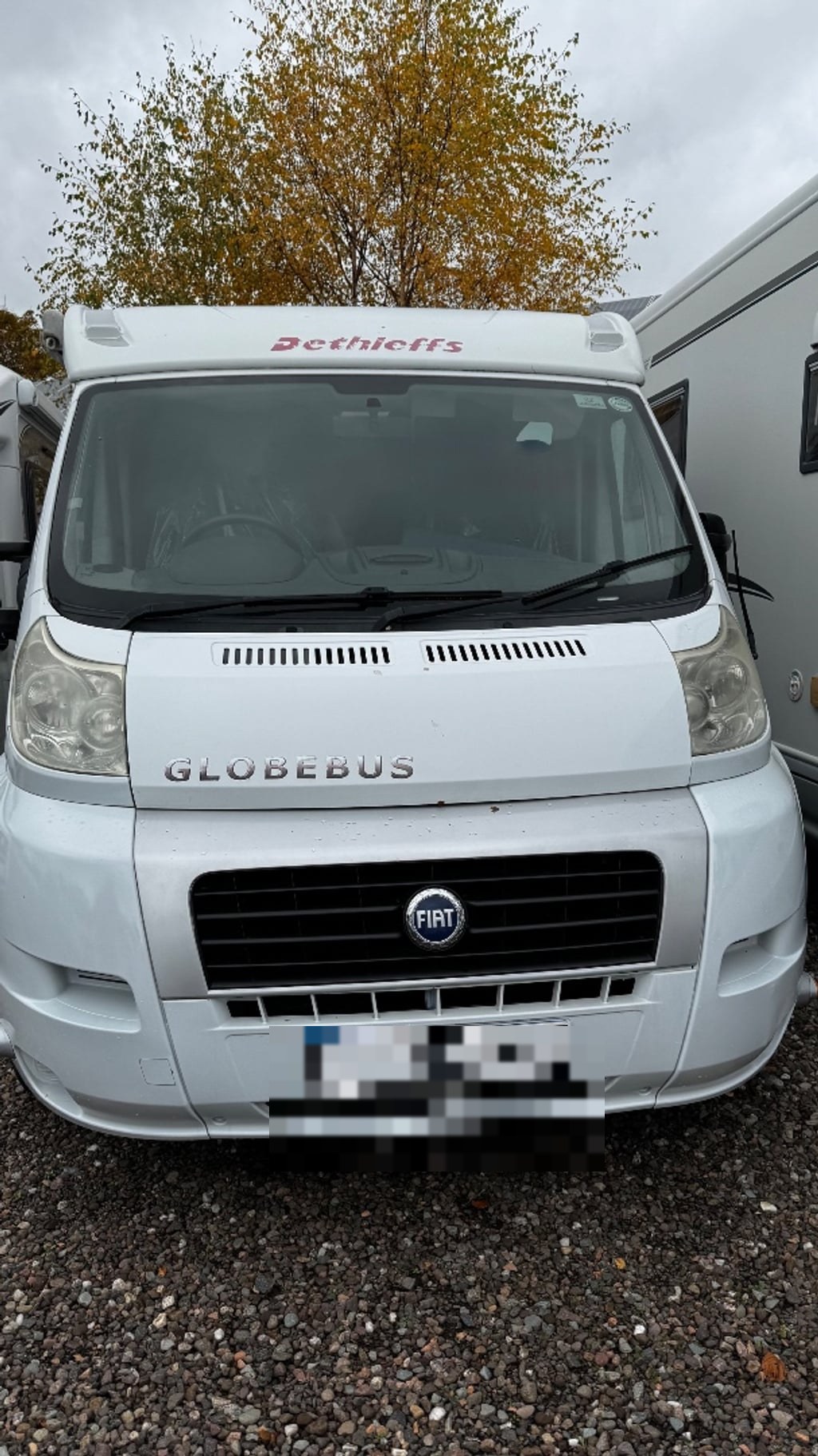 Front view of the white Dethleffs Globebus on its Fiat Ducato base, showing the Fiat grille badge and 'Globebus' lettering (number plate digitally obscured)