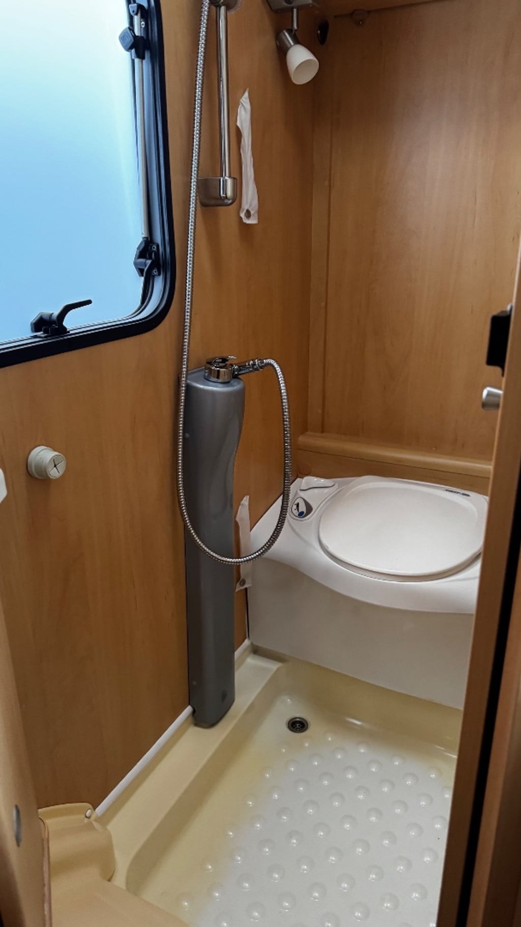 The wet room of the Dethleffs Globebus with a wall-mounted shower, cassette toilet and a light wood-panelled finish
