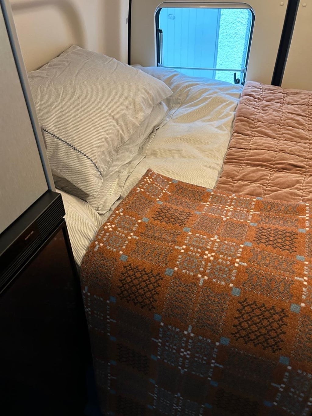 The made-up rear fixed double bed in the Hymer Free S 600, with cream pillows and a patterned throw beside a window
