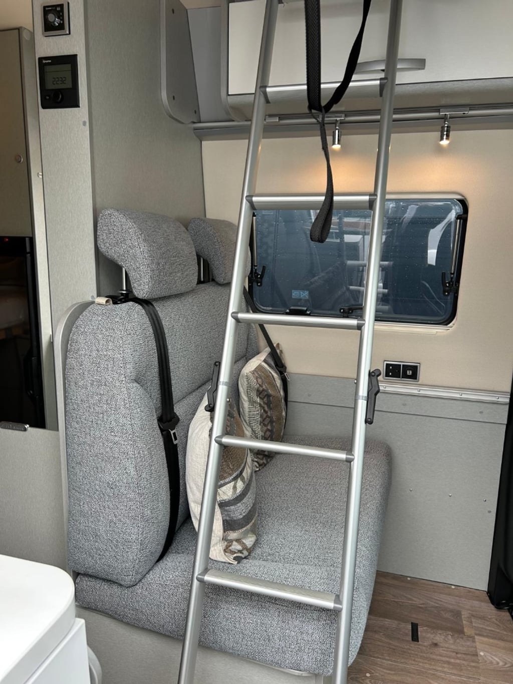 Interior of the Hymer Free S 600 showing the ladder up to the pop-up roof bed beside the upholstered seating