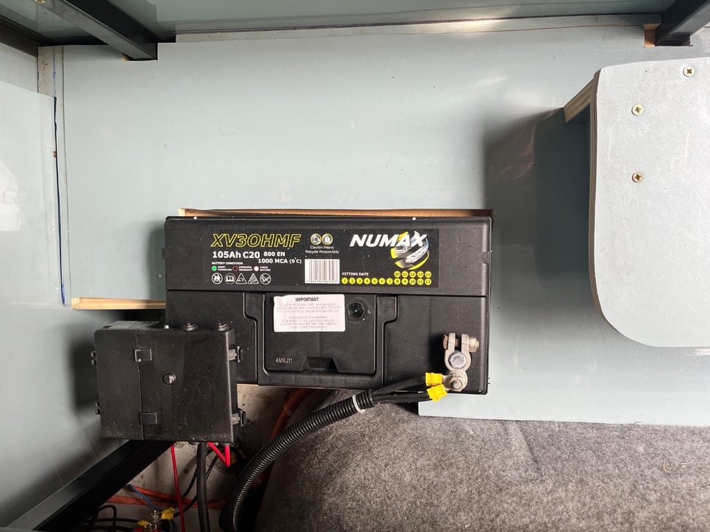 The leisure battery installation inside the self-converted campervan, showing the battery and wiring in a fitted compartment
