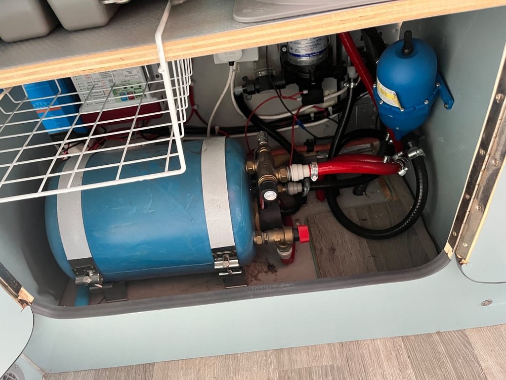 The campervan's water system with pressurised pump, pipework and tank visible under a lifted floor panel
