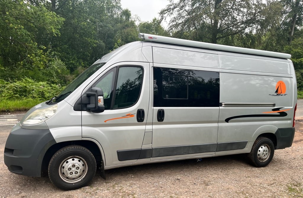 Side profile of the silver self-converted Peugeot Boxer L3H2 campervan parked on a woodland track