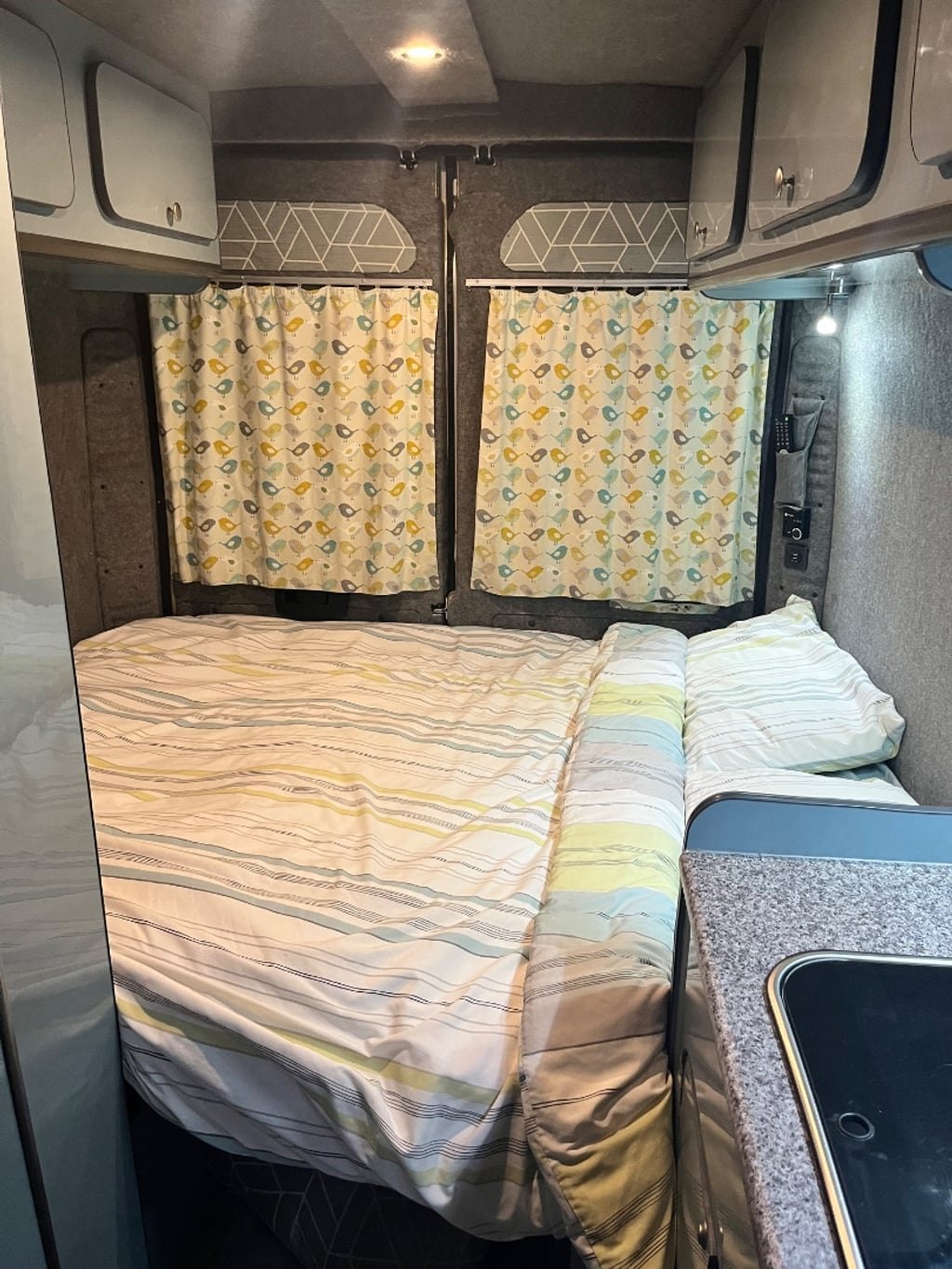 The campervan's rear seats converted into a made-up double bed with pillows and a duvet, curtains drawn