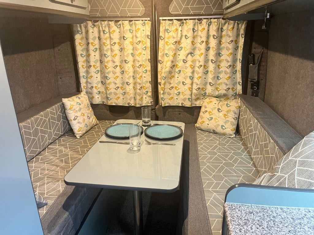 The campervan's dinette with a pedestal table between two upholstered bench seats and patterned curtains