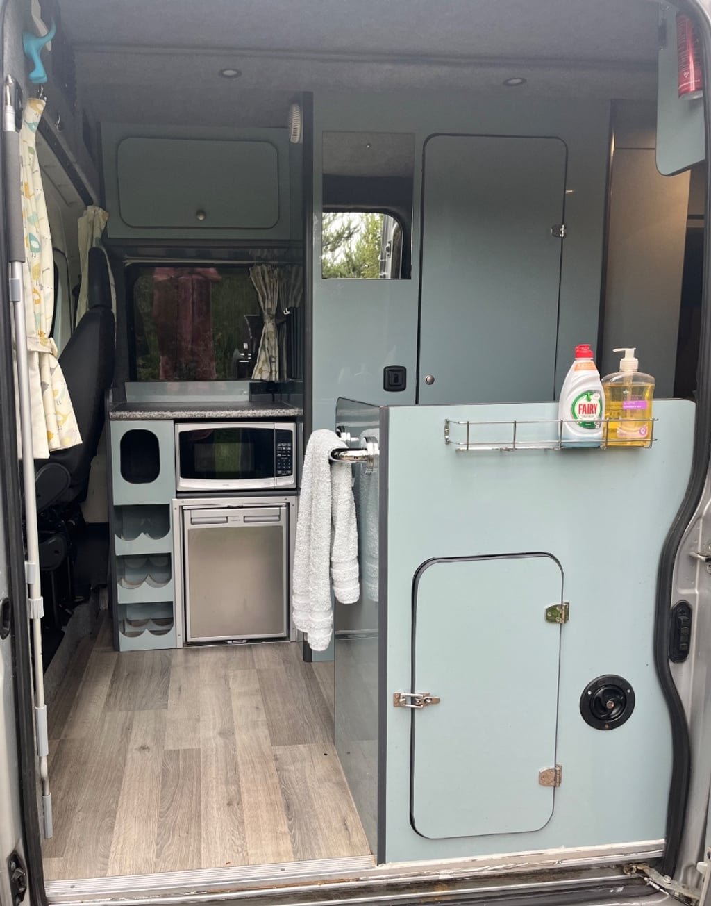 The interior of the campervan looking forward from the rear doors, past the galley unit and wardrobe toward the cab