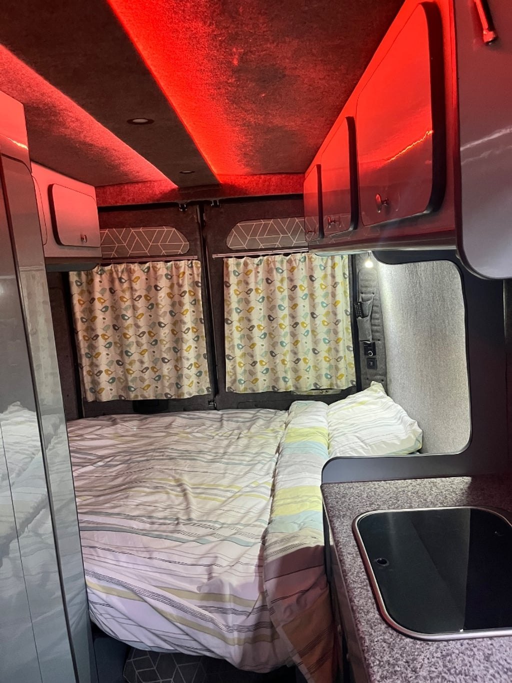 The campervan interior at night with a colour-changing LED strip light casting red light over the made-up bed