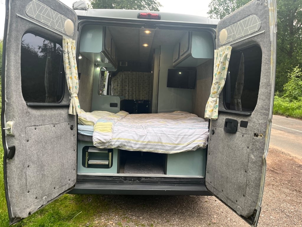 The rear doors of the campervan open onto the bed made up across the back, with a storage space beneath it