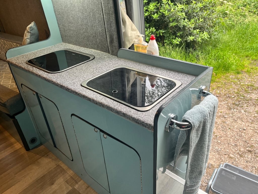The campervan's galley kitchen unit with a two-ring hob and worktop, seen through the open side door