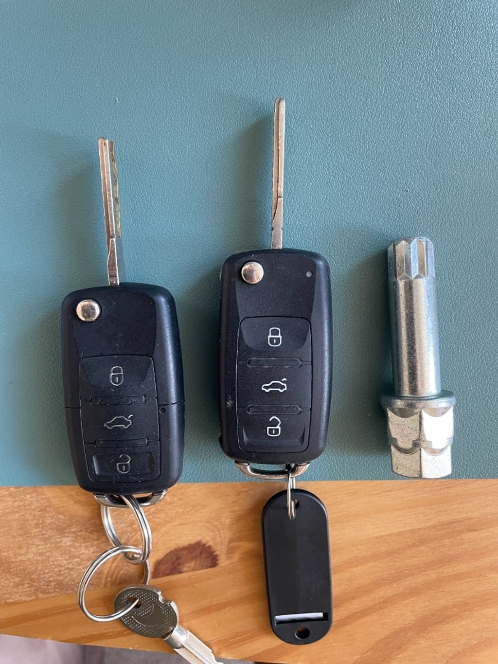 Two VW key fobs and a locking wheel nut key laid out on a wooden surface