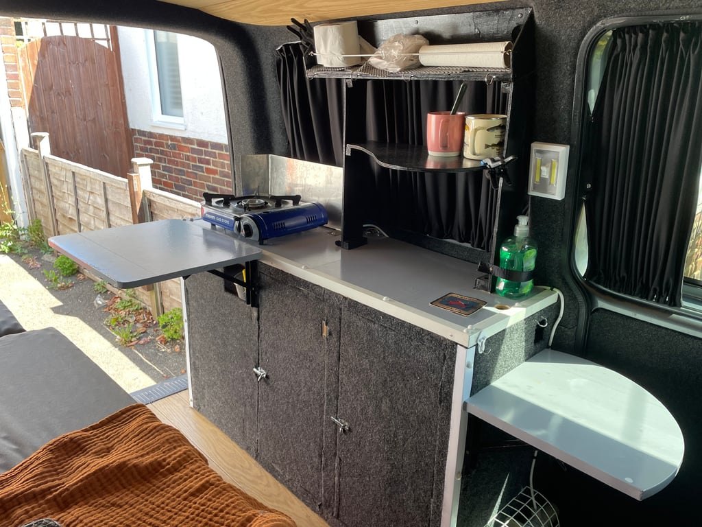 The campervan's kitchen unit with a gas burner on the worktop and a fold-out table extended
